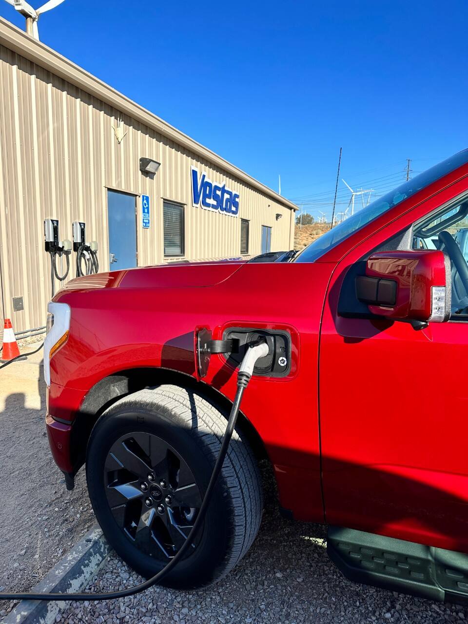 A red Ford F-150 Lightning charges at building with Vestas on the side.